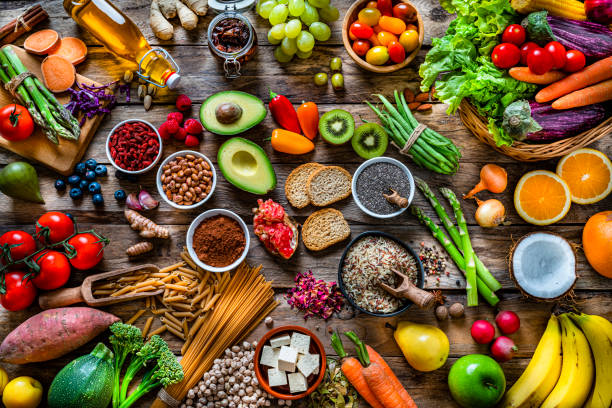 Vegan food backgrounds: large group of fruits, vegetables, cereals and spices shot from above Vegan food backgrounds: large group of multicolored fresh fruits, vegetables, cereals and spices shot from above on wooden background. The composition includes green apple, kiwi, pear, pomegranate, orange, coconut, banana, grape, berries, ginger, almonds, pistachio, olive oil, olives, goji berries, chia seeds, pinto beans, nutmeg, rosemary, radish, tomatoes, carrot, kale, avocado, onion, rice, cocoa powder, sweet potato, wholegrain pasta, tofu, lettuce, corn, broccoli, pepper, asparagus, green beans, among others. High resolution 42Mp studio digital capture taken with SONY A7rII and Zeiss Batis 40mm F2.0 CF lens dietary fiber photos stock pictures, royalty-free photos & images