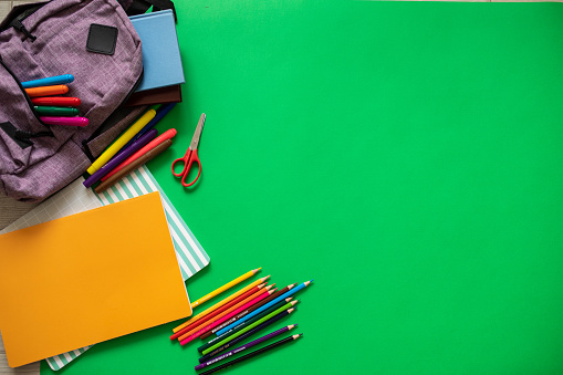 Backpack with school supplies on green background, directly above shot
