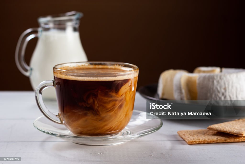 Black coffee with cream poured over. A cup of hot american black coffee with cream poured over. Tasty breackfast with creamy Camembert cheese on natural white wooden table. Coffee - Drink Stock Photo