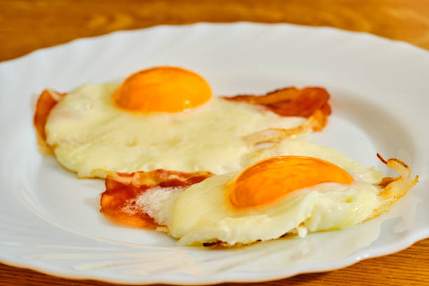 istock Two tasty fried egg with bacon on wihte plate on wooden table 1278945973