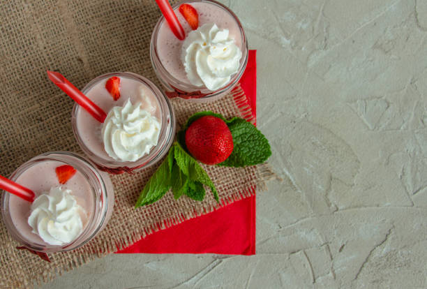 three jars of delicious milk strawberry cocktail with whipped cream on a concrete background with strawberries and mint - vitality food food and drink berry fruit imagens e fotografias de stock