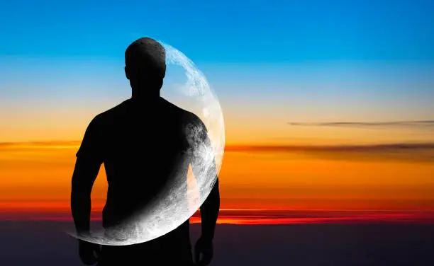 Photo of Silhouette of man with transparent crescent or moon on body in front blue sky during sunset, concept picture about space, astronomy and astrology