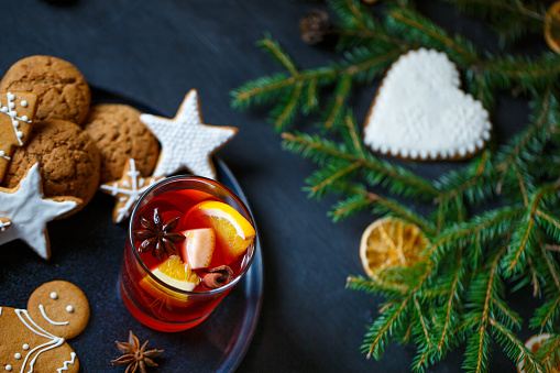 On the black surface of the table is a plate of ginger cookies and a glass of hot mulled wine