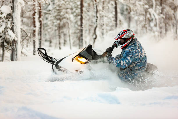 el jinete haciendo un giro a la deriva en una moto de nieve en una superficie de nieve profunda al aire libre sobre un fondo de bosque nevado. - motoesquí fotografías e im�ágenes de stock