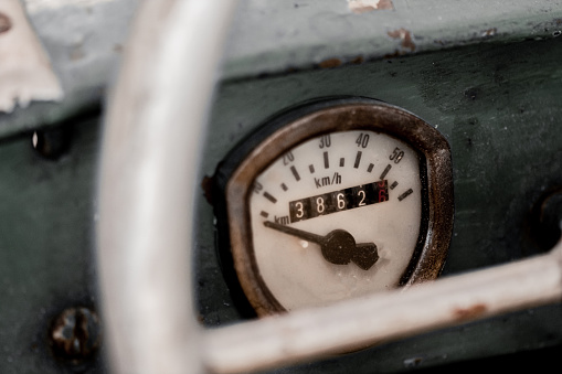 Old rusty speedometer and odometer on a vintage car or wreck viewed through the steering wheel in close up showing the dial or gauge