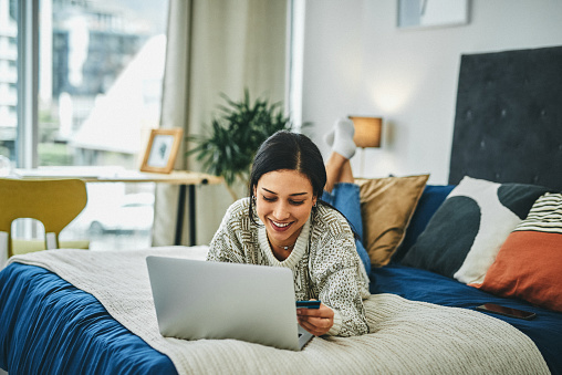 Shot of a young woman using a laptop and credit card on the bed at home