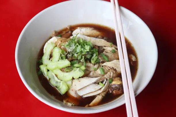 Photo of Thai style of chicken noodle with bitter gourd in white bowl on red table background.