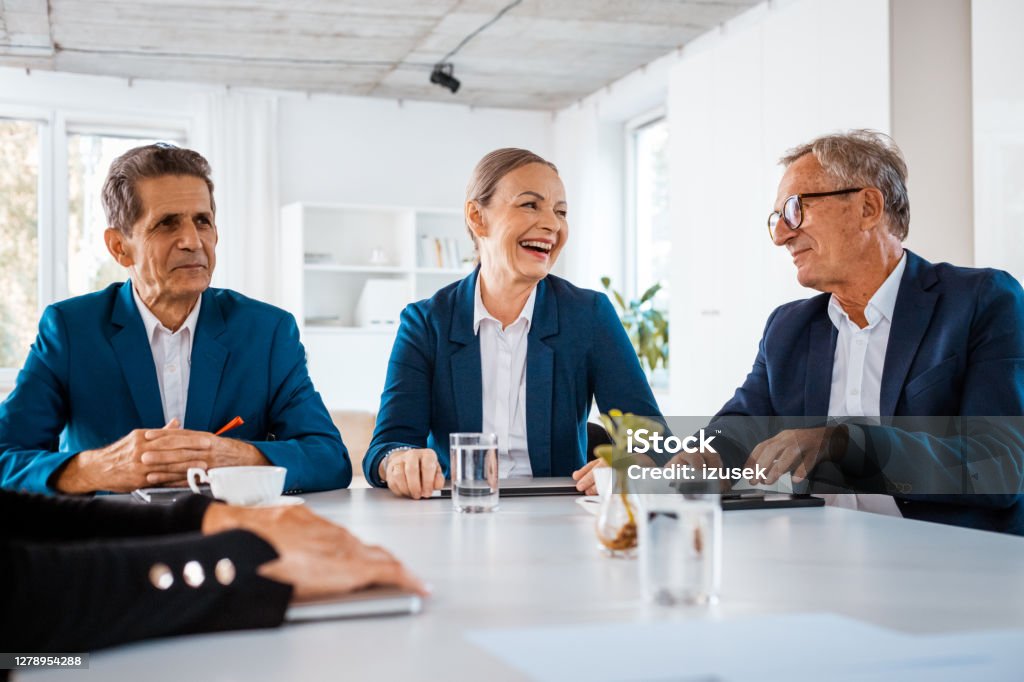 Happy senior business people during meeting Senior businesswoman and businessmen wearing elegant suits sitting at the table in the office and discussing during business meeting. Corporate Governance Stock Photo