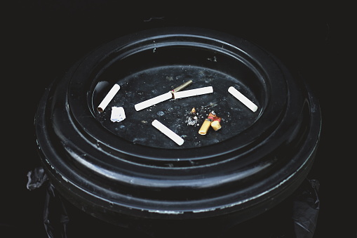 Ashtray with cigarette butts close-up. Dark blurred background, no focus, smoking harm concept