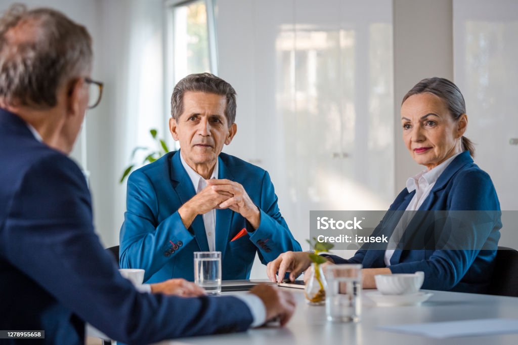 Senior business people in the office Senior businesswoman and businessmen wearing elegant suits sitting at the table in the office and discussing. Corporate Governance Stock Photo