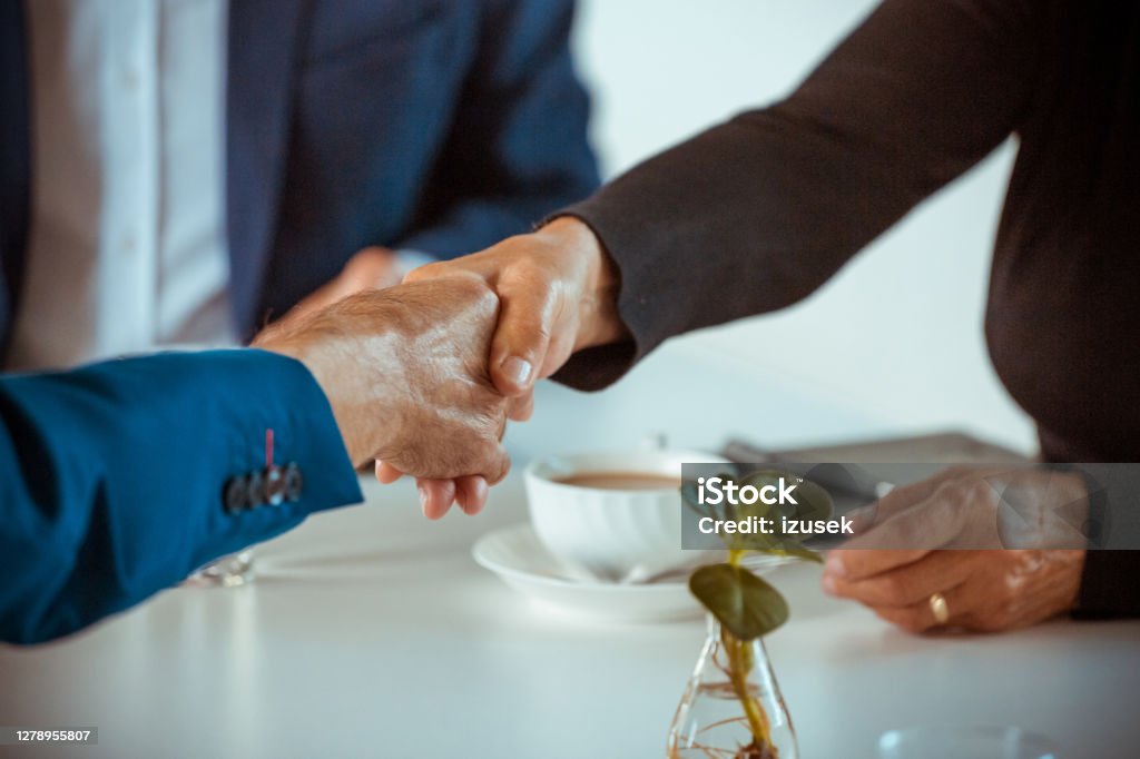 Senior business people shaking hands Senior businesswoman and businessmen sitting at the table in the office and shaking hands during business meeting. Close up of hands, unrecognizable people. Part Of Stock Photo