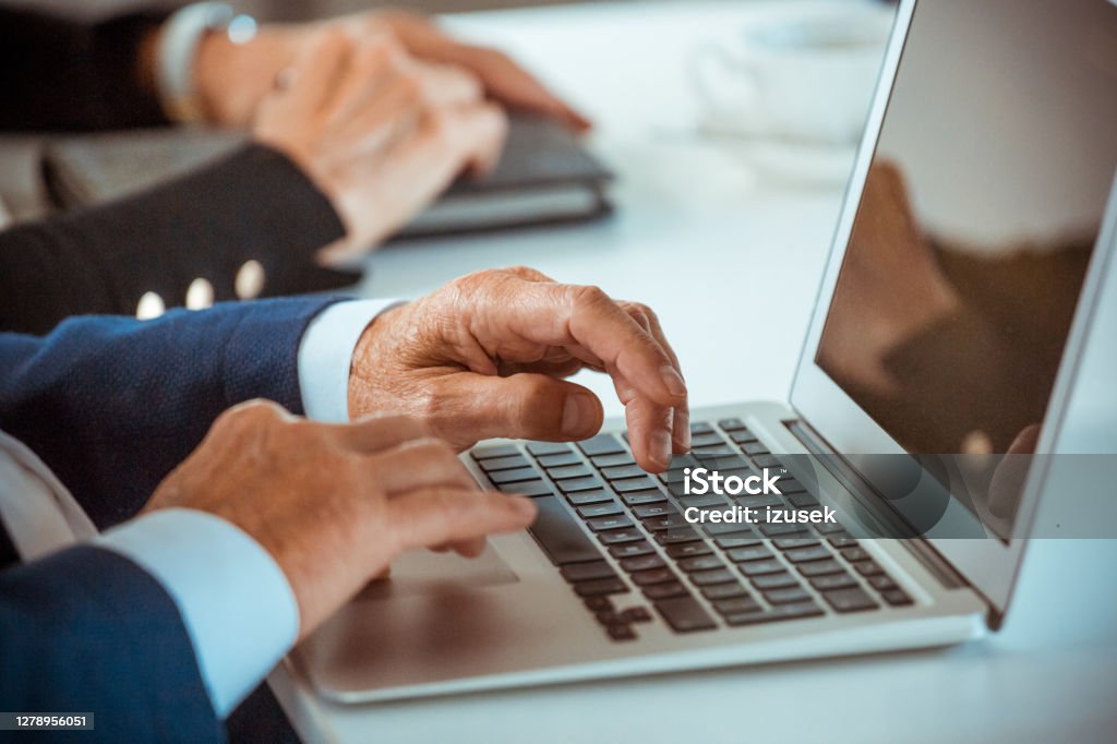 Senior businessmen using laptop Senior entrepreneur wearing elegant suits sitting at the table in the office, working on laptops. Close up on hands, unrecognizable person. Senior Men Stock Photo