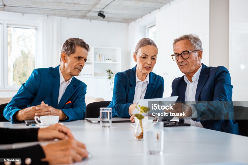 Shareholder discussing contract during business meeting Senior businesswoman and businessmen wearing elegant suits sitting at the table in the office and discussing contract during business meeting. Corporate Governance Stock Photo