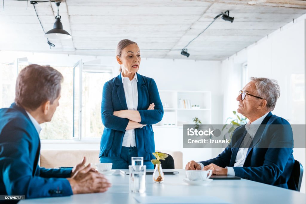 Shareholders during business meeting Senior businesswoman and businessmen wearing elegant suits sitting at the table in the office and discussing during business meeting. Shareholder Stock Photo