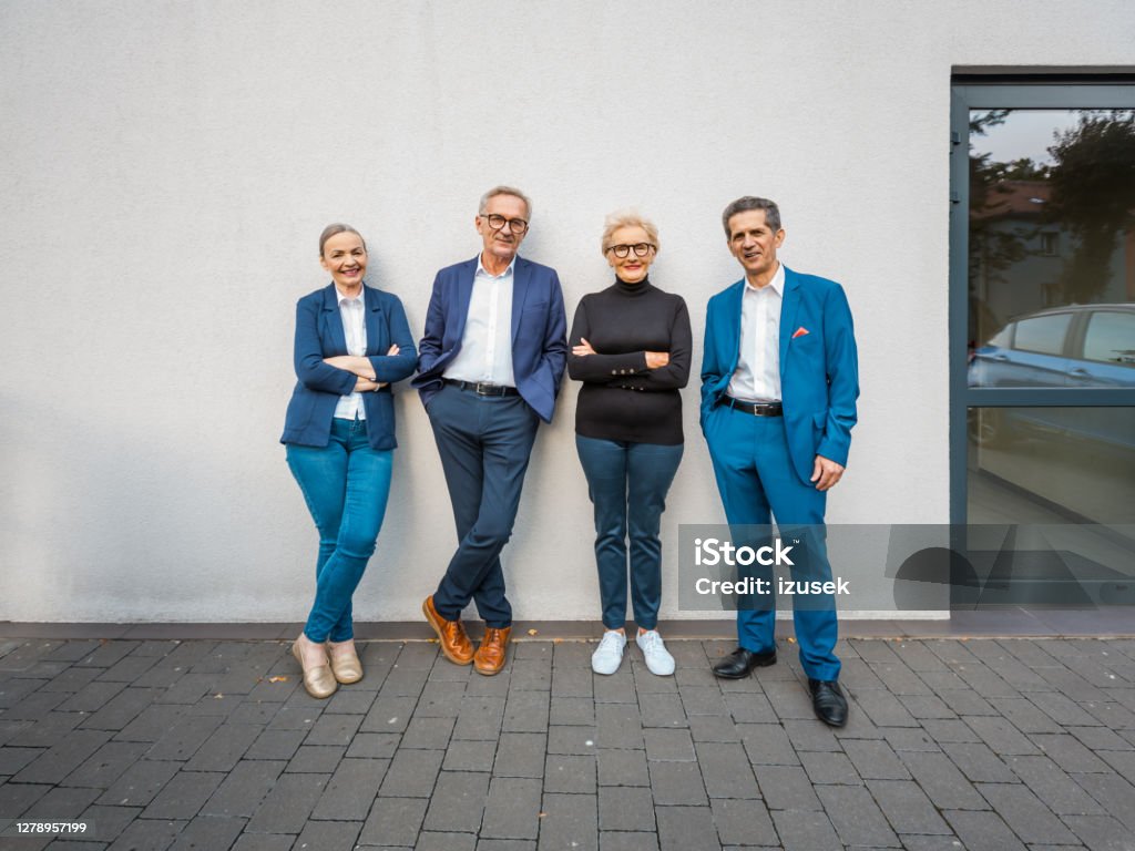 Successful business people Portrait of senior businesswomen and businessmen wearing elegant suits standing outdoors in front of office and smiling at camera. Outdoors Stock Photo