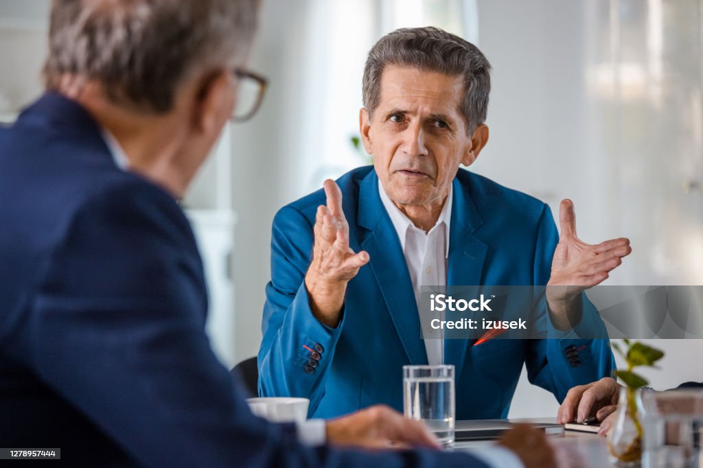 Two senior businessmen in the office Elderly man wearing elegant suit sitting at the table in the office and talking with his business partner. Two People Stock Photo