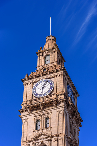 The clock tower of the Melbourne GPO building against a blue sky, light cloud cover