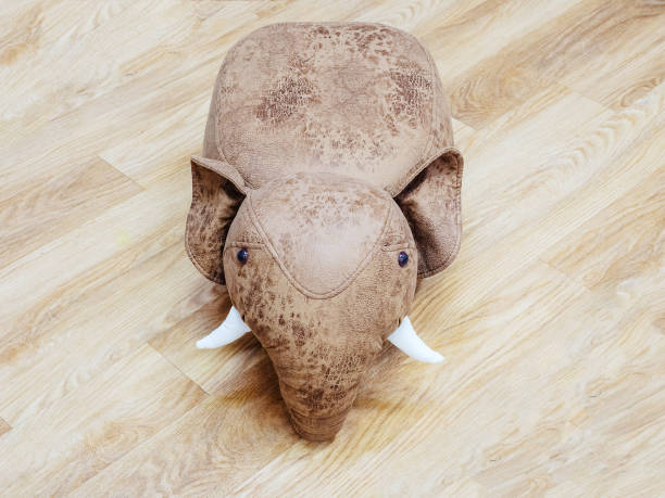 Toy brown soft leather elephant with white tusks on wood floor