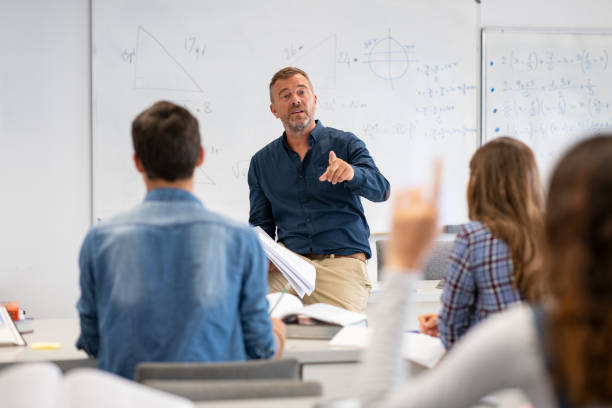 Student raising hand in classroom at the high school Professor pointing at college student with hand raised in classroom. Student raising a hand with a question for the teacher. Lecturer teaching in class while girl have a question to do during a math lesson. interrogation woman stock pictures, royalty-free photos & images