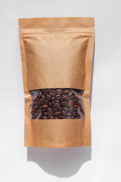 白い背景に影が隔離されたコーヒー豆のトップビューを持つ茶色のクラフト紙のポーチバッグ。食品包装フラットレイ - coffee package ストックフォトと画像