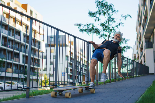Portrait of mature man riding skateboard outdoors in city, falling down and accident concept.