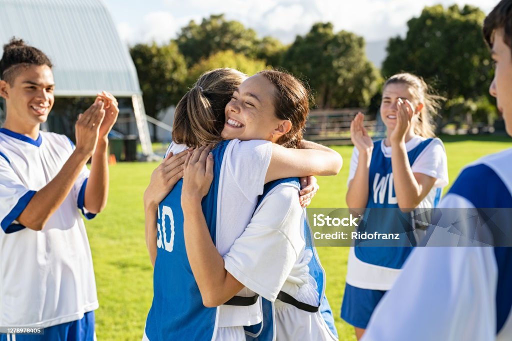 Girls soccer players celebrating victory Smiling football players hugging on field after scoring a goal. Cheerful soccer teammates embracing while players clapping hands on victory. Successful girl soccer players embracing on field and celebrating after winning the match. Sport Stock Photo