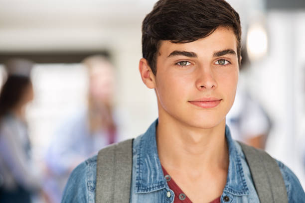 Happy student guy at college Portrait of handsome high school student standing in school hallway and looking at camera. Intelligent college guy with backpack smiling with copy space. Confident university young man standing in campus. 16 17 years stock pictures, royalty-free photos & images