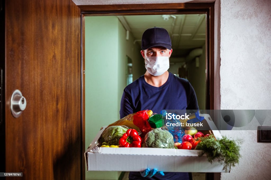 Groceries home delivery Young man delivering groceries during coronavirus pandemic, wearing protective masks and gloves. A Helping Hand Stock Photo