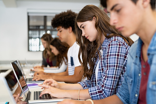 Group of high school students using laptop in classroom