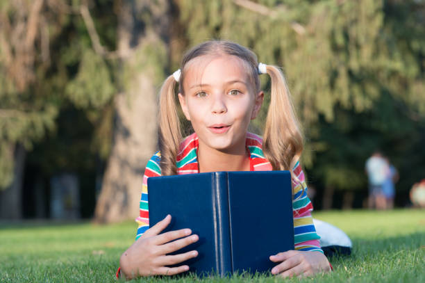 istock Adorable bookworm. School time. Developing caring learners who are actively growing and achieving. Little child reading book. Schoolgirl reading stories relaxing green lawn. Cute pupil enjoy reading 1278979723