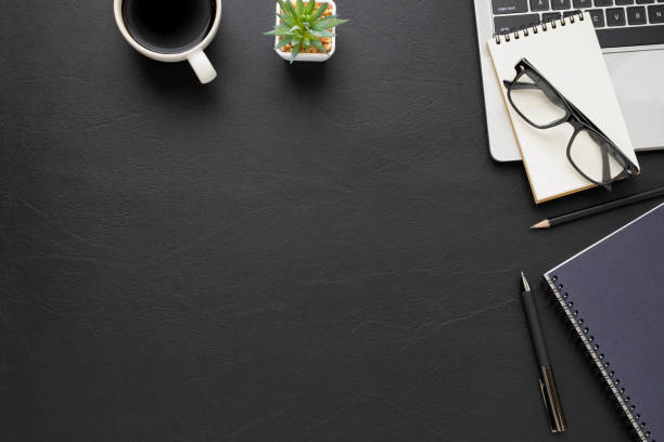 istock Top view above of Black leather office desk table with keyboard, notebook and coffee cup with equipment office supplies. Business and finance concept. Workplace, Flat lay with blank copy space. 1278979814