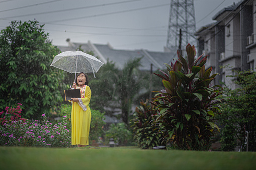 Asia Chinese girl holding umbrella and moon cake box walking in public park rainy day. She enjoying mid-autumn festival.