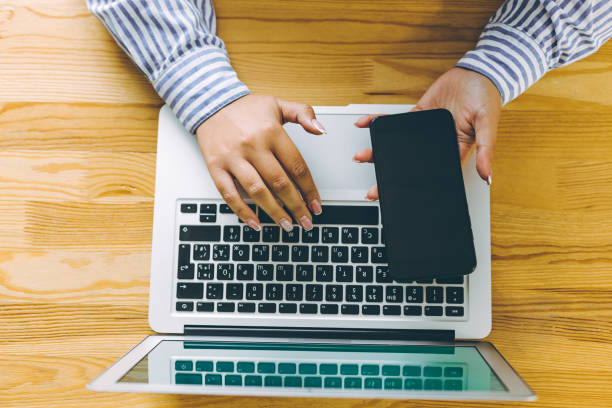 istock Top-view of hand using smartphone at office desk while typing on laptop . 1278983183