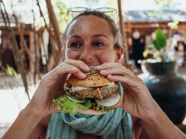Woman eating vegan burger in cool cafe Girl in hipster cafe eating yummy burger. Tropical vacations, eating by the beach bagan archaeological zone stock pictures, royalty-free photos & images