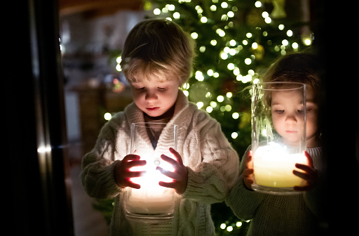 Portrait of happy small girl and boy indoors at home at Christmas, holding candles.