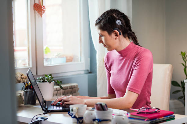 Beautiful young woman with cochlear implant Young woman with cochlear implant studying at home.For better learning results she using modern technology. assistive technology stock pictures, royalty-free photos & images