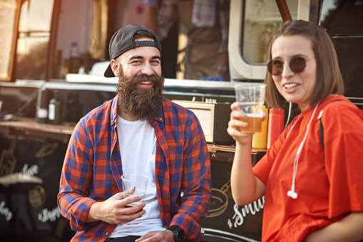 Hipster couple chilling out with beer in front of food truck