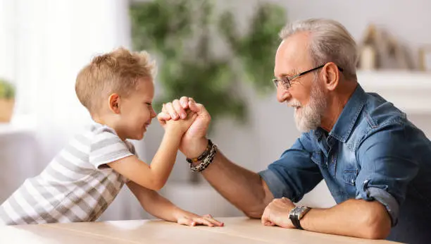 Side view of senior bearded man arm wrestling with happy boy while spending time at home together