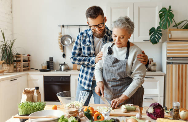 happy housewife with adult son preparing healthy dinner at home - family mother domestic life food imagens e fotografias de stock