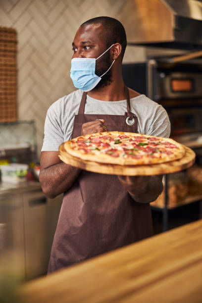 istock Afro American man in protective face mask holding pepperoni pizza 1278994332