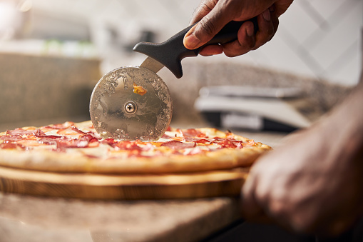 Close up of male hand slicing freshly baked pizza with round cutter wheel