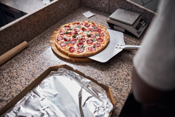 Close up of male hand holding pizza peel with delicious freshly baked pepperoni pizza