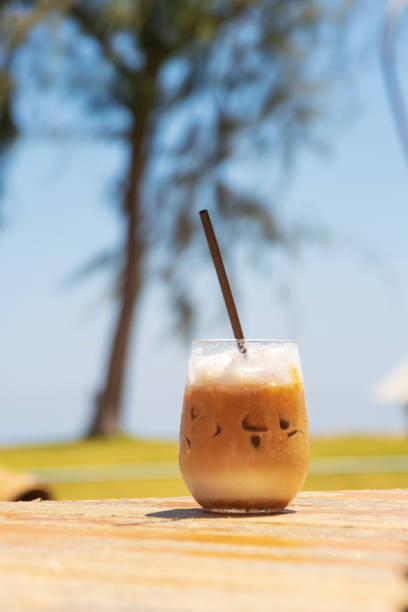 istock Iced coffee on wooden table on summer beach with pine tree and blue sky background. 1278995628