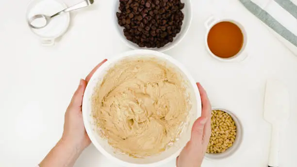 Photo of Chocolate Chip Cookie batter close up in a bowl on white kitchen table, woman hands, view from above