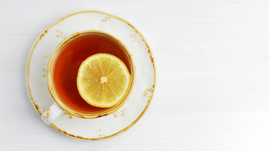 Cup of tea with a slice of lemon on white wooden table. Top view. Copyspace.