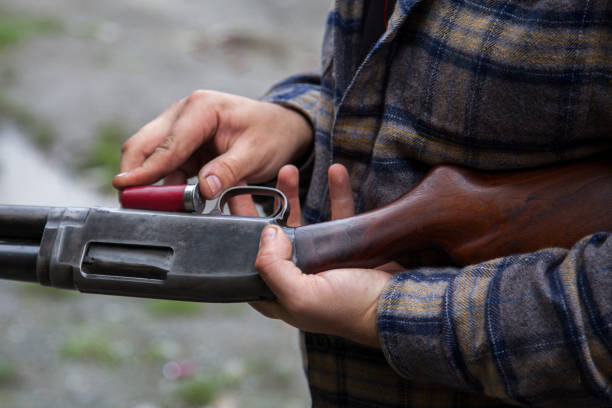 Close up of man loading a red shotgun shell into the magazine of his gun stock photo