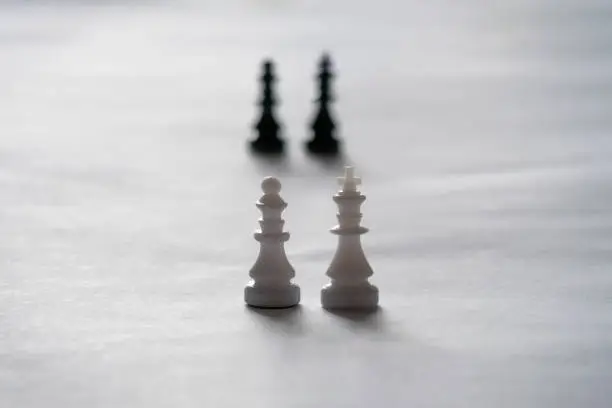 Kings and queens on white background. Plastic black and white chess pieces from travel set. Selective focus.