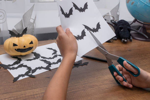 les mains de l’enfant sont coupées de silhouettes de papier de chauves-souris noires, citrouille avec le visage peint se trouvent près. - face paint child animal little boys photos et images de collection