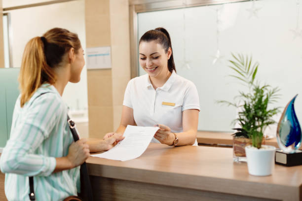 Happy receptionist talking to a customer at health spa. Happy massage therapist communicating with a customer at reception desk at the spa. receptionist stock pictures, royalty-free photos & images
