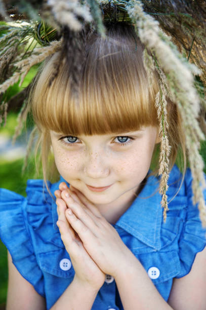 linda garota ruiva com sardas e uma coroa de ervas de verão na cabeça olha para a câmera com olhos azuis. jovem linda menina 7-10 anos de idade na natureza - 7 10 years - fotografias e filmes do acervo